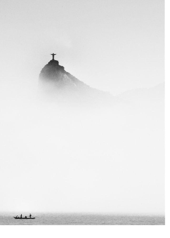 Christ the Redeemer poster with a black and white view of the statue in fog and a boat below