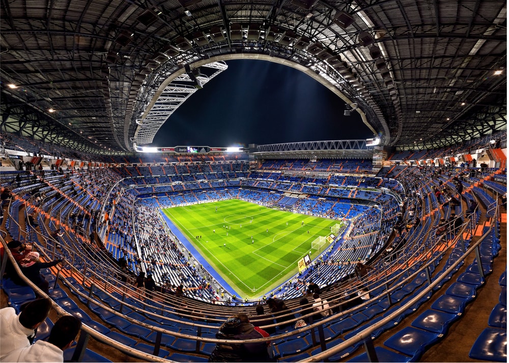 Football stadium poster with a night view of a green pitch and blue seats under a large roof
